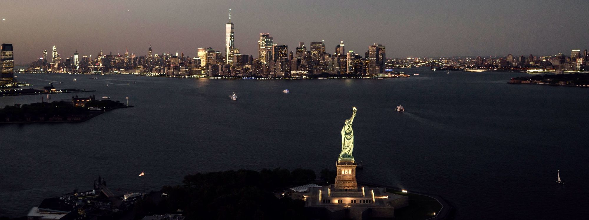 Aerial view of the Statue of Liberty with the Manhattan skyline behind it at dusk